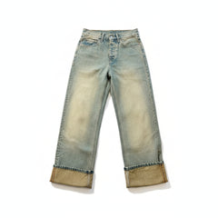 A pair of light-wash blue jeans laid flat on a polished marble floor, featuring a faded yellow-tan wash and rolled cuffs.