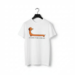 A white short-sleeve crewneck t-shirt hanging on a black hanger, featuring a cartoon dachshund graphic and the text 'IT'S GOING TO BE A LONG DAY' printed on the front.