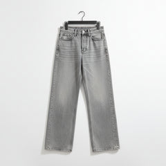 Light gray washed denim jeans with a straight-leg or wide-leg cut, laid flat on a dark marble-patterned surface. The jeans are shown hanging from a black hanger, with the cuffs rolled up to reveal the inner seam detail.